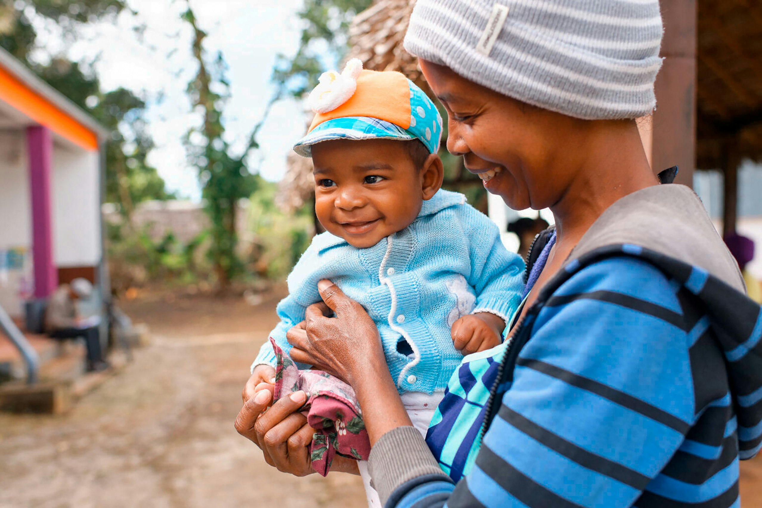 A smiling child in his mother's arms, waiting for the vaccination and nutrition room to open.